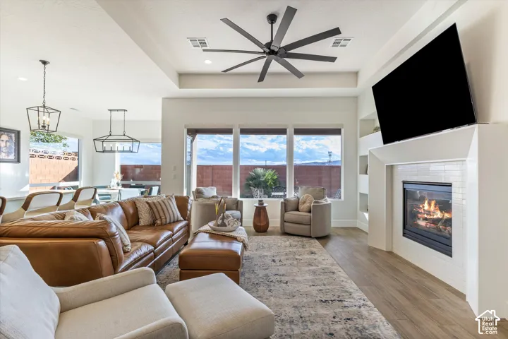 Living area featuring a tray ceiling, large-blade ceiling fan, wood-finish flooring, built-in shelving, and a tiled fireplace surround
