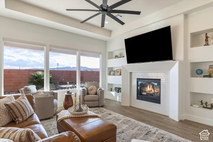 Tray ceiling with a multi-blade ceiling fan, expansive windows, built-in wall niches, and a tile-surround fireplace