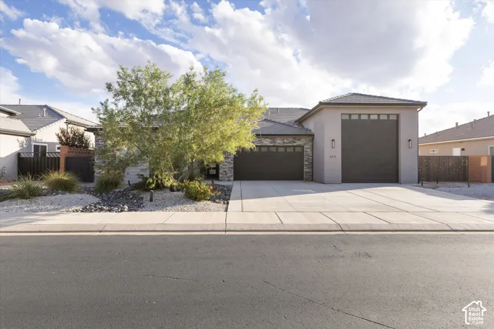 Single-story exterior featuring a stone veneer facade, concrete driveway, and a multi-car garage with dark, panel-style doors