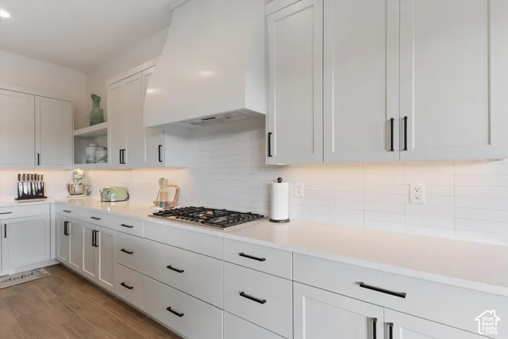 Kitchen featuring light-colored cabinetry with matte black hardware, stone-finish countertops, a custom hood range, white subway tile backsplash, and wood-finish flooring