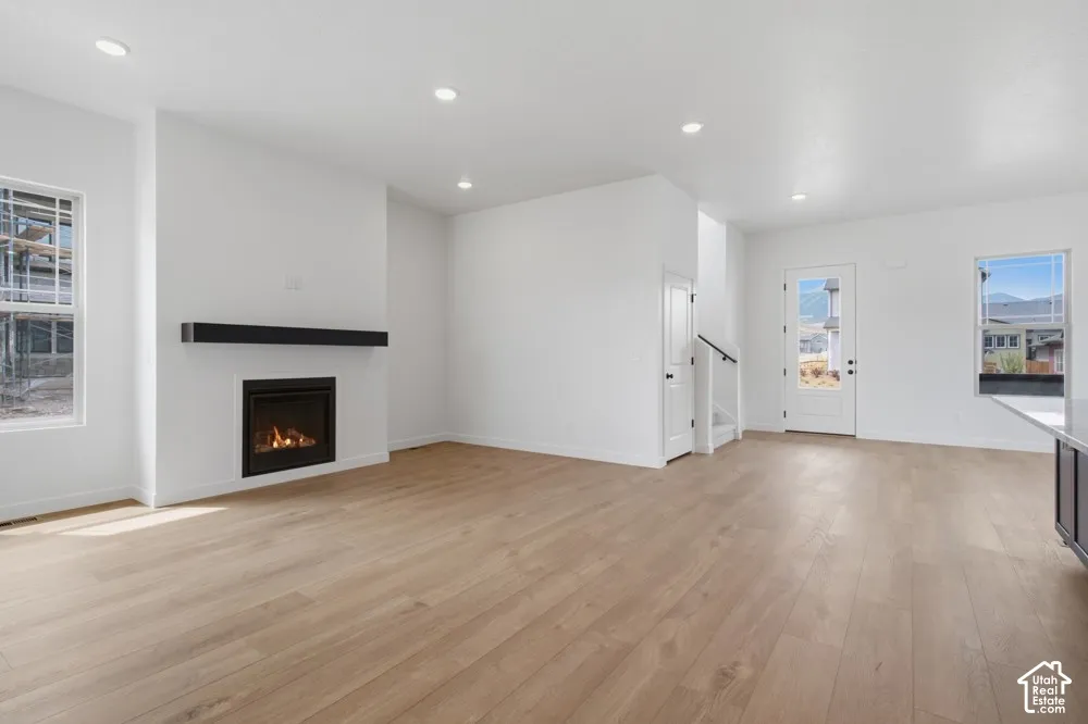 Open interior featuring light-tone wood-finish flooring, recessed lighting, and a linear gas fireplace with a prominent mantel
