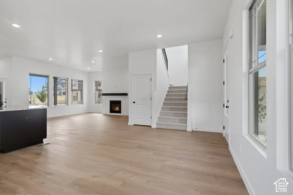 Open-concept interior featuring wood-finish flooring, recessed lighting, a fireplace with a mantel, and large windows with ample natural light