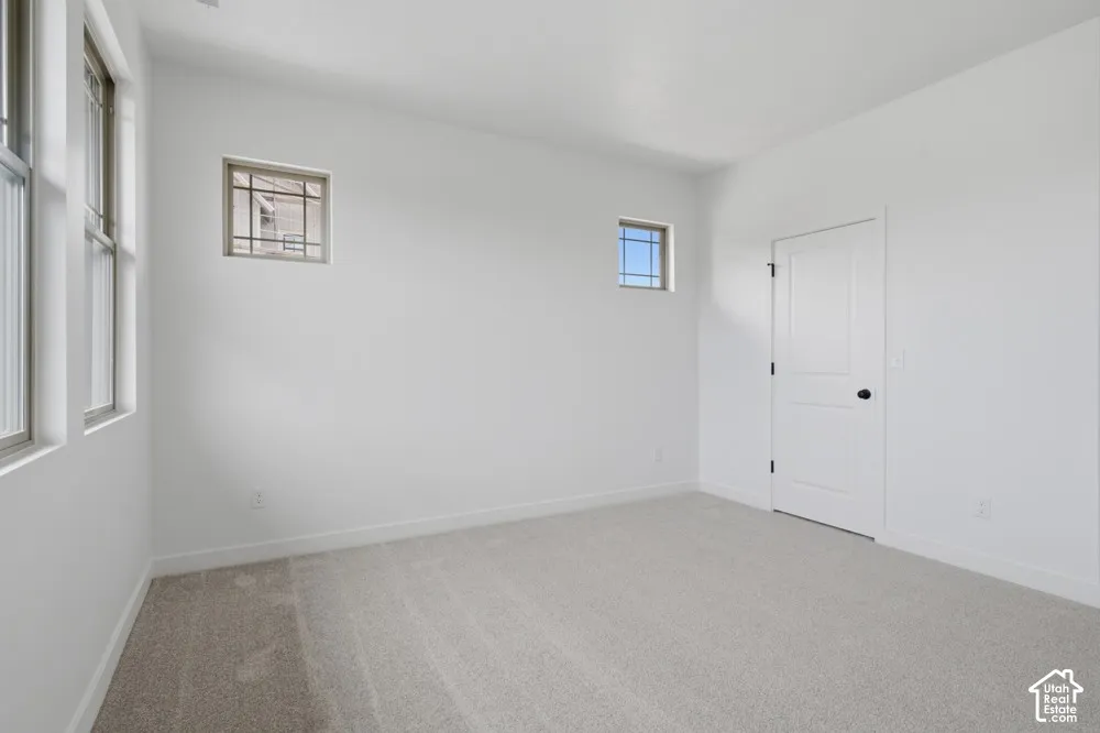 Neutral-toned carpeted flooring, two square transom windows with grid detailing, two rectangular windows, and a white paneled interior door