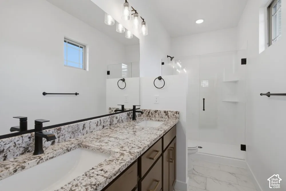 Double vanity with stone-look countertops, undermount sinks, matte black fixtures, and walk-in shower with glass enclosure