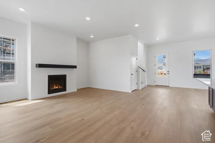 Open interior featuring light-tone wood-finish flooring, recessed lighting, and a linear gas fireplace with a prominent mantel