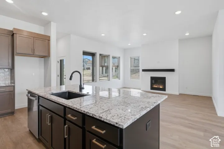 Kitchen island with stone-finish countertop, undermount sink, and matte black faucet, featuring wood-finish flooring, recessed lighting, and a fireplace with a mantel