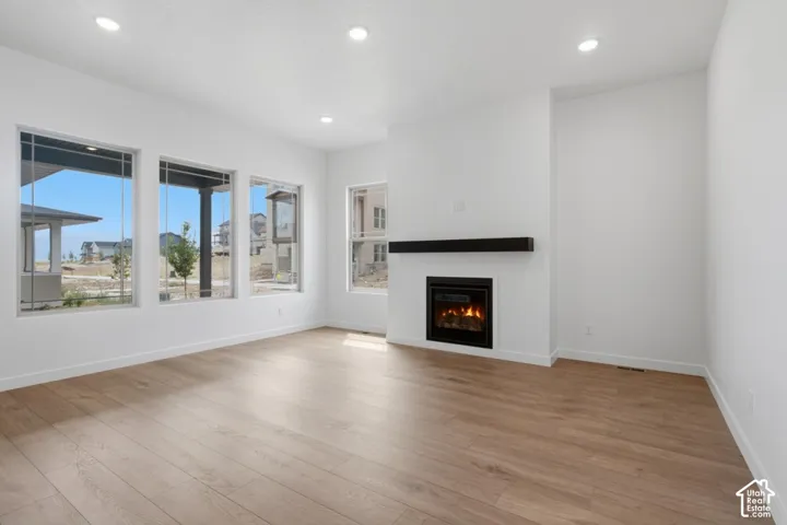 Open-concept living space featuring wood-finish flooring, recessed lighting, expansive windows, and a gas fireplace with a prominent mantel