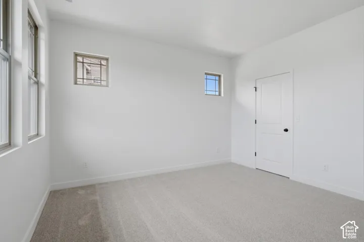 Neutral-toned carpeted flooring, two square transom windows with grid detailing, two rectangular windows, and a white paneled interior door