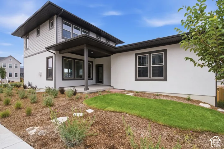 Contemporary exterior featuring a covered patio, two-tone siding, dark-trimmed window frames, and professional landscaping with a grass lawn and stone pavers
