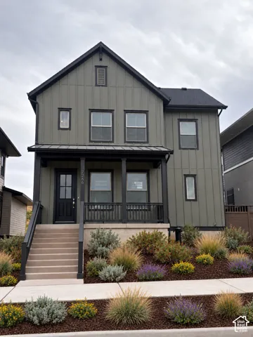 Two-story exterior featuring board-and-batten siding, a covered front porch with metal roofing, and structured landscaping with ornamental grasses and shrubs