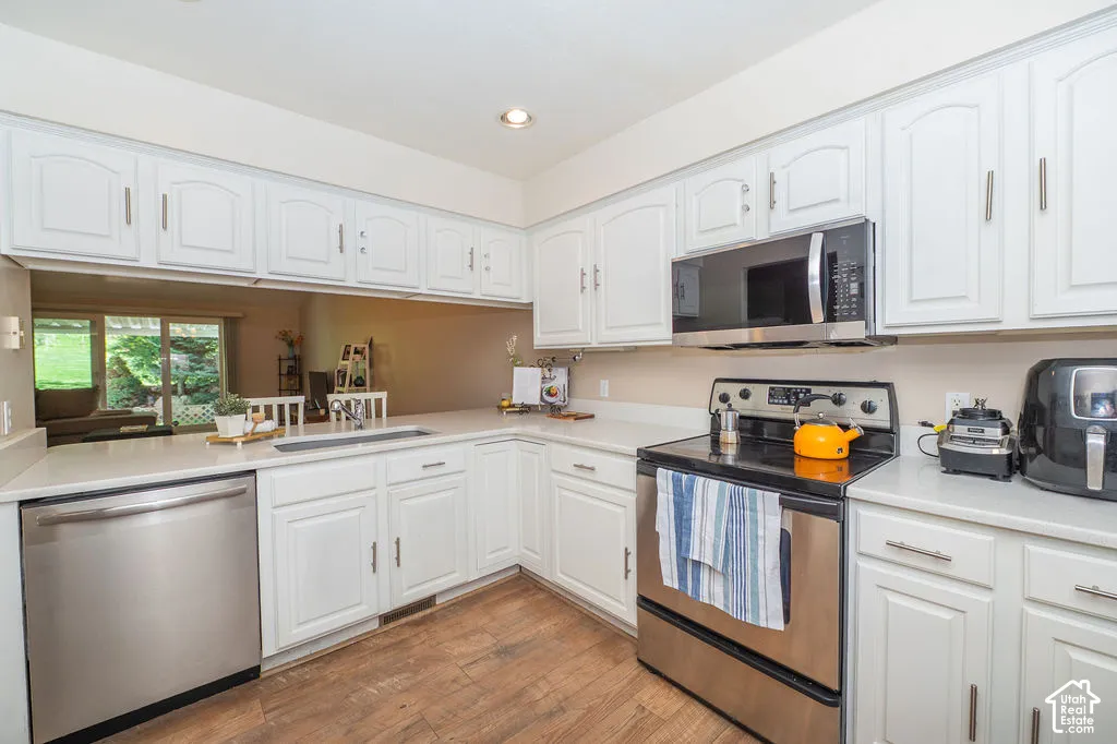 Kitchen featuring white cabinetry, solid-surface countertops, wood-finish flooring, and stainless steel appliances including an over-the-range microwave
