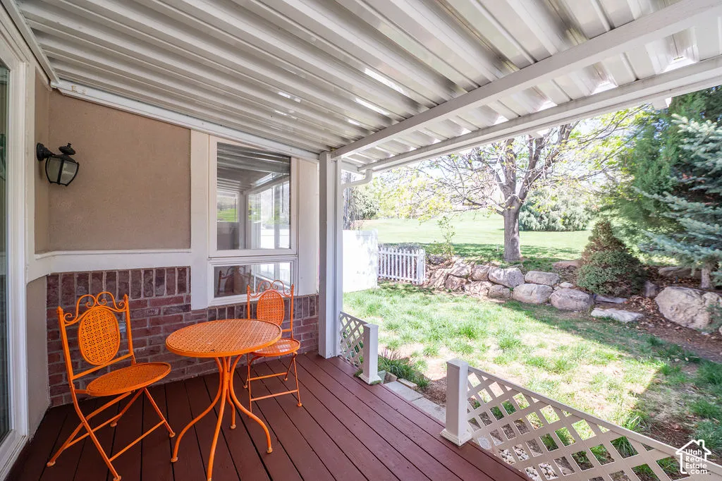 Covered patio featuring wood-finish decking, white lattice railing, brick masonry exterior accents, and attached exterior light fixture