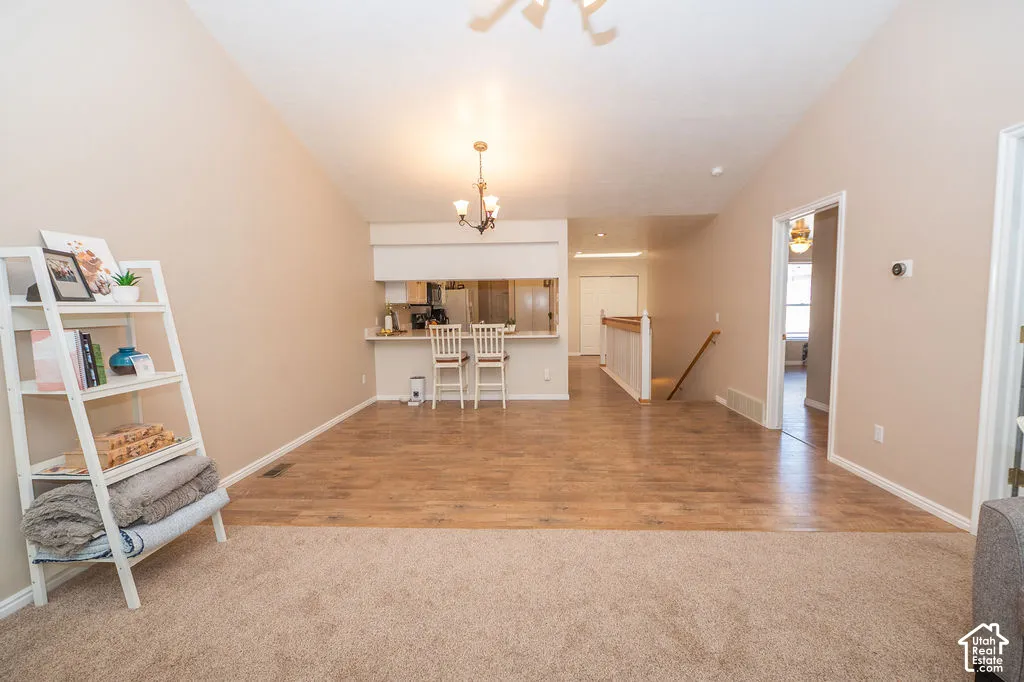 Vaulted ceilings, wood-finish flooring, and pass-through kitchen counter featuring a hanging light fixture and integrated wooden railing