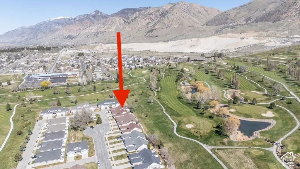Aerial perspective of a multi-unit residential property featuring a pitched shingle roof, positioned near an expansive golf course and mountain backdrop