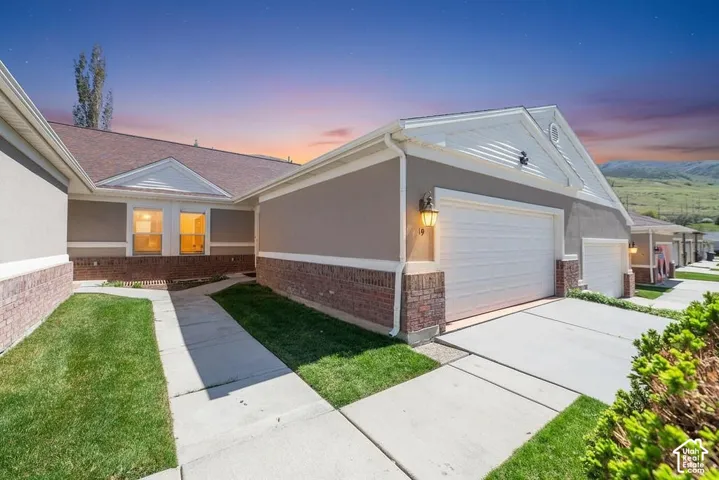 Multi-gabled exterior featuring a combination of stucco and brick siding, dual-car garage, concrete driveway, and a paved walkway