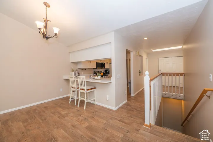 Kitchen featuring a breakfast bar, wood-finish flooring, white cabinetry, decorative chandelier, and a wood-railed staircase