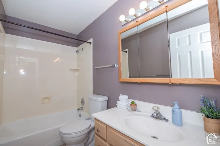 Bathroom featuring a vanity with a white countertop and integrated sink, wood-finish cabinetry, a tri-fold medicine cabinet, four-light vanity fixture, and a tub-shower combination with surround