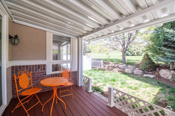 Covered patio featuring wood-finish decking, white lattice railing, brick masonry exterior accents, and attached exterior light fixture