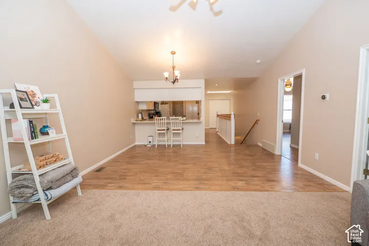 Vaulted ceilings, wood-finish flooring, and pass-through kitchen counter featuring a hanging light fixture and integrated wooden railing