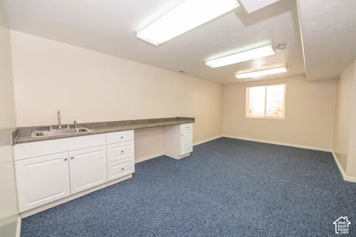 Built-in cabinetry with white shaker-style doors, stone-composite countertop, stainless steel drop-in sink with chrome faucet, and recessed rectangular overhead lighting