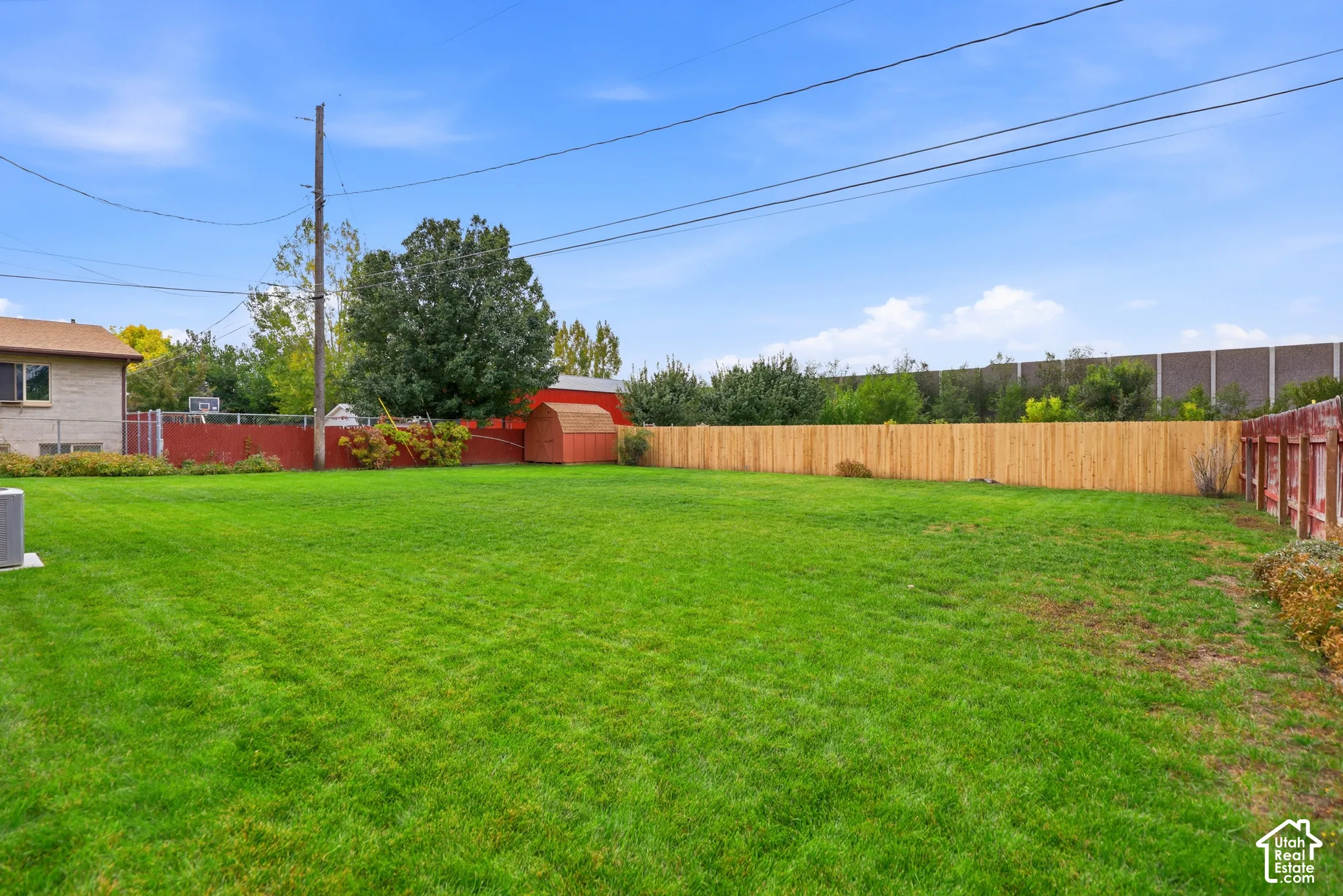Expansive backyard featuring a large grass lawn, wood fencing, mature trees, and a detached shed