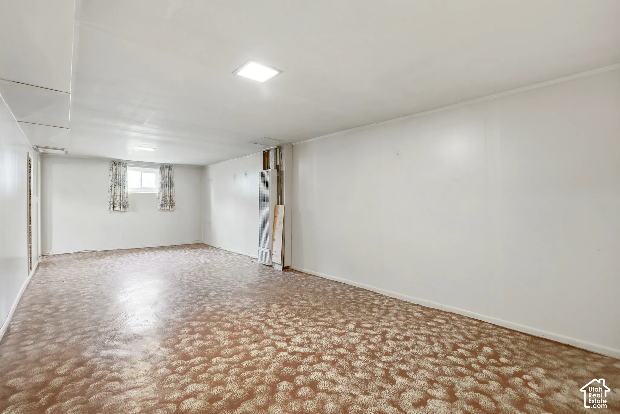 Finished interior space featuring smooth wall surfaces, recessed ceiling lighting, a singular window, and a wall-mounted heating unit