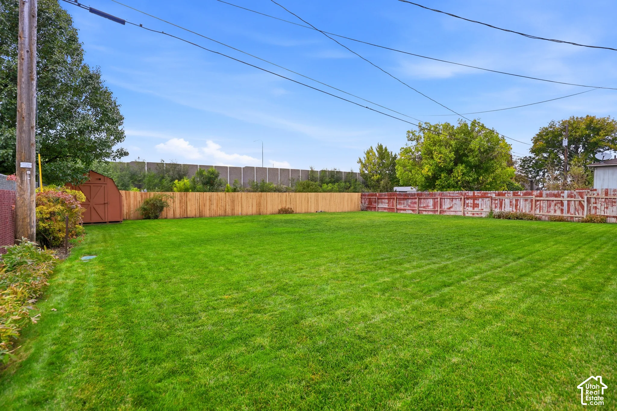 Expansive backyard featuring a manicured lawn, a detached storage shed, and perimeter wood fencing