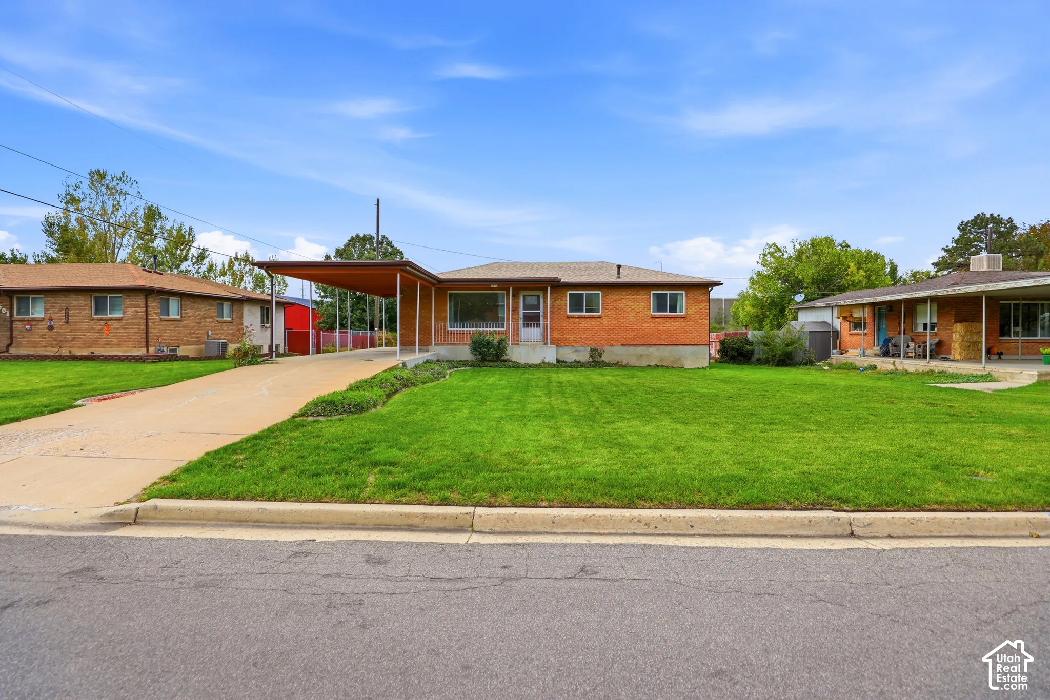 Mid-century brick exterior featuring a covered carport, concrete driveway, and expansive lawn