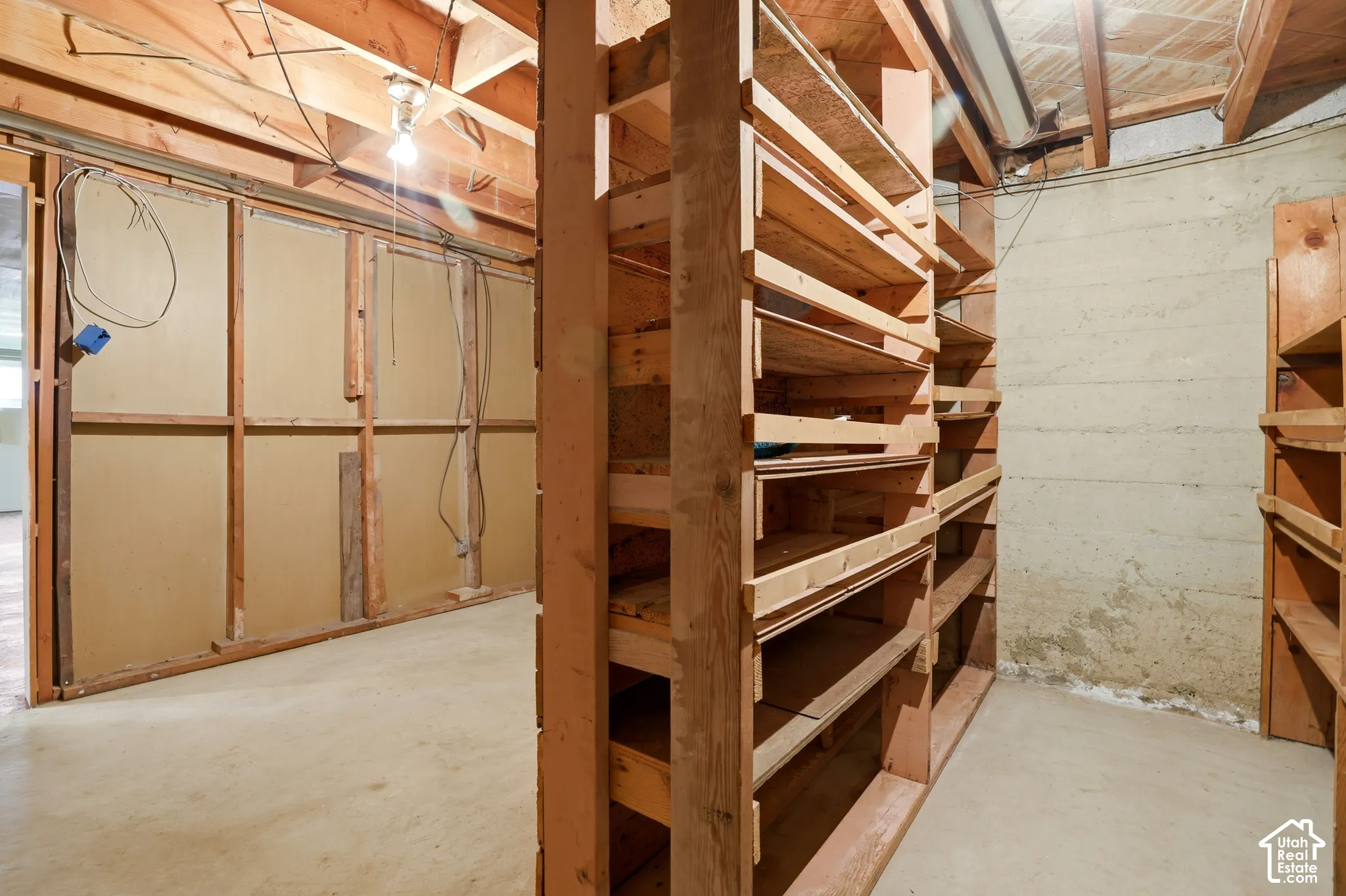Unfinished utility space featuring exposed wooden structural beams, concrete flooring, masonry walls, and extensive built-in wood shelving units