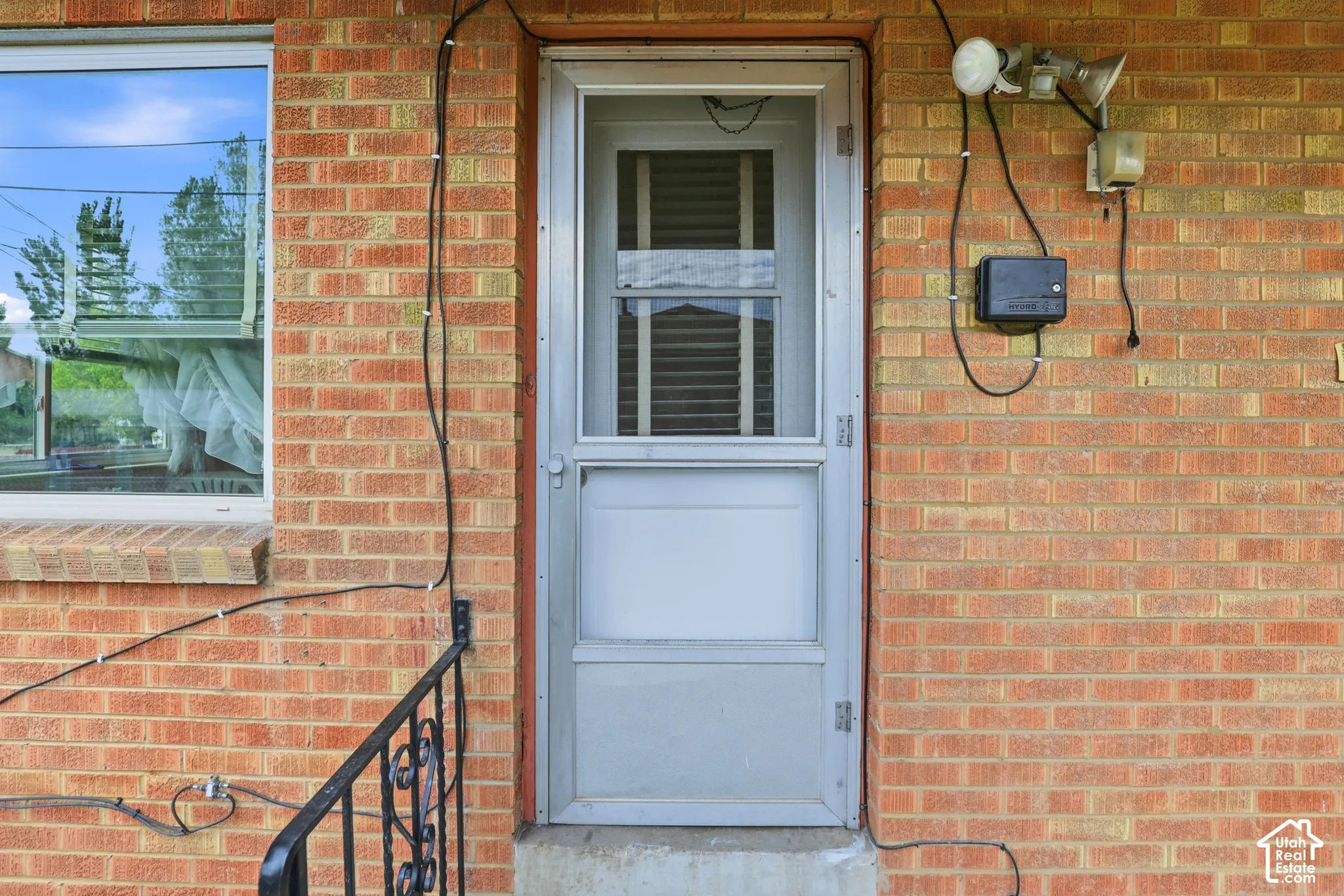 Exterior featuring a red-tone brick facade, metal storm door, and decorative black metal handrail