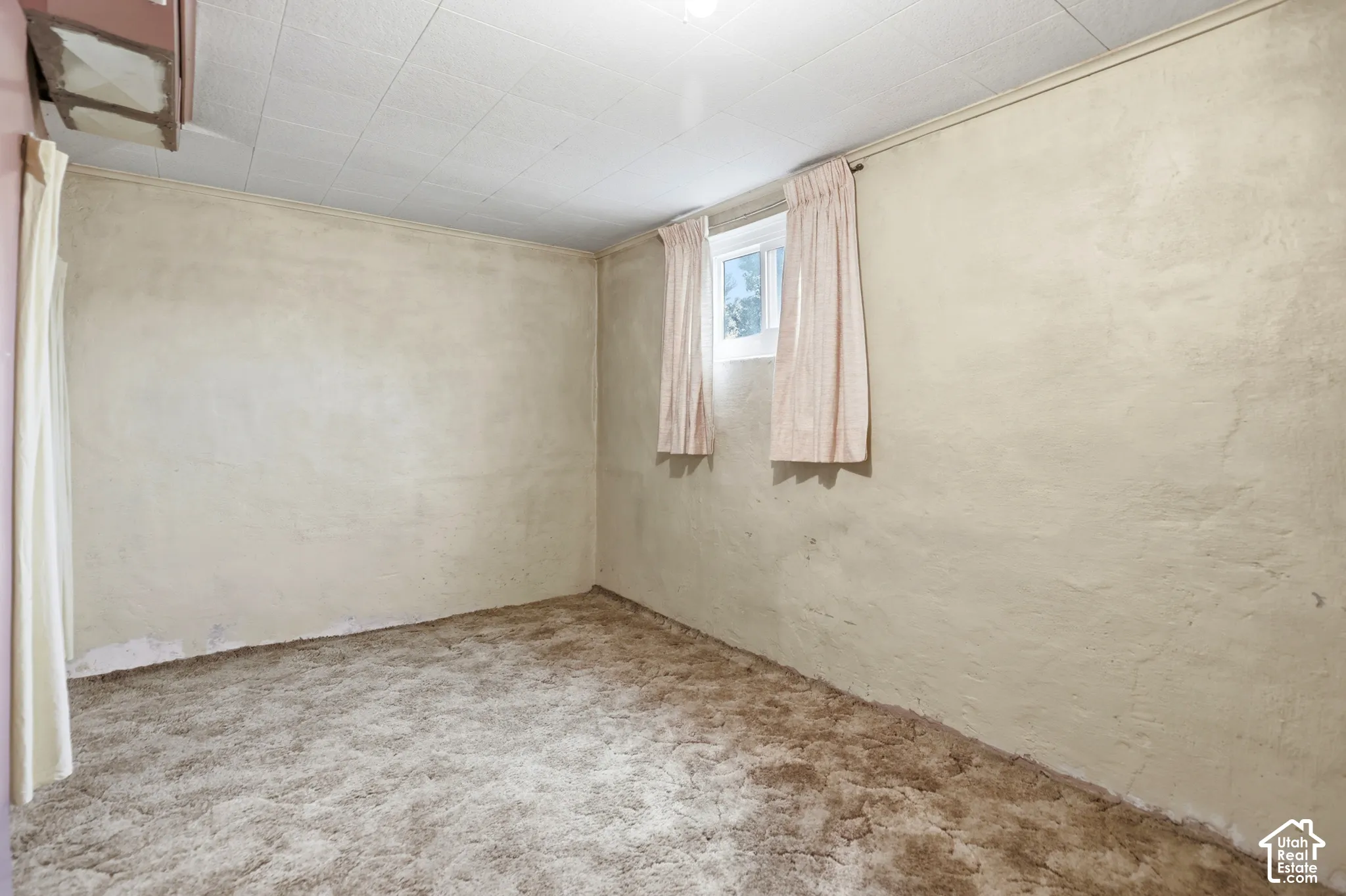 Textured wall finishes, carpeted flooring, and a single pane window with fixed rod hardware