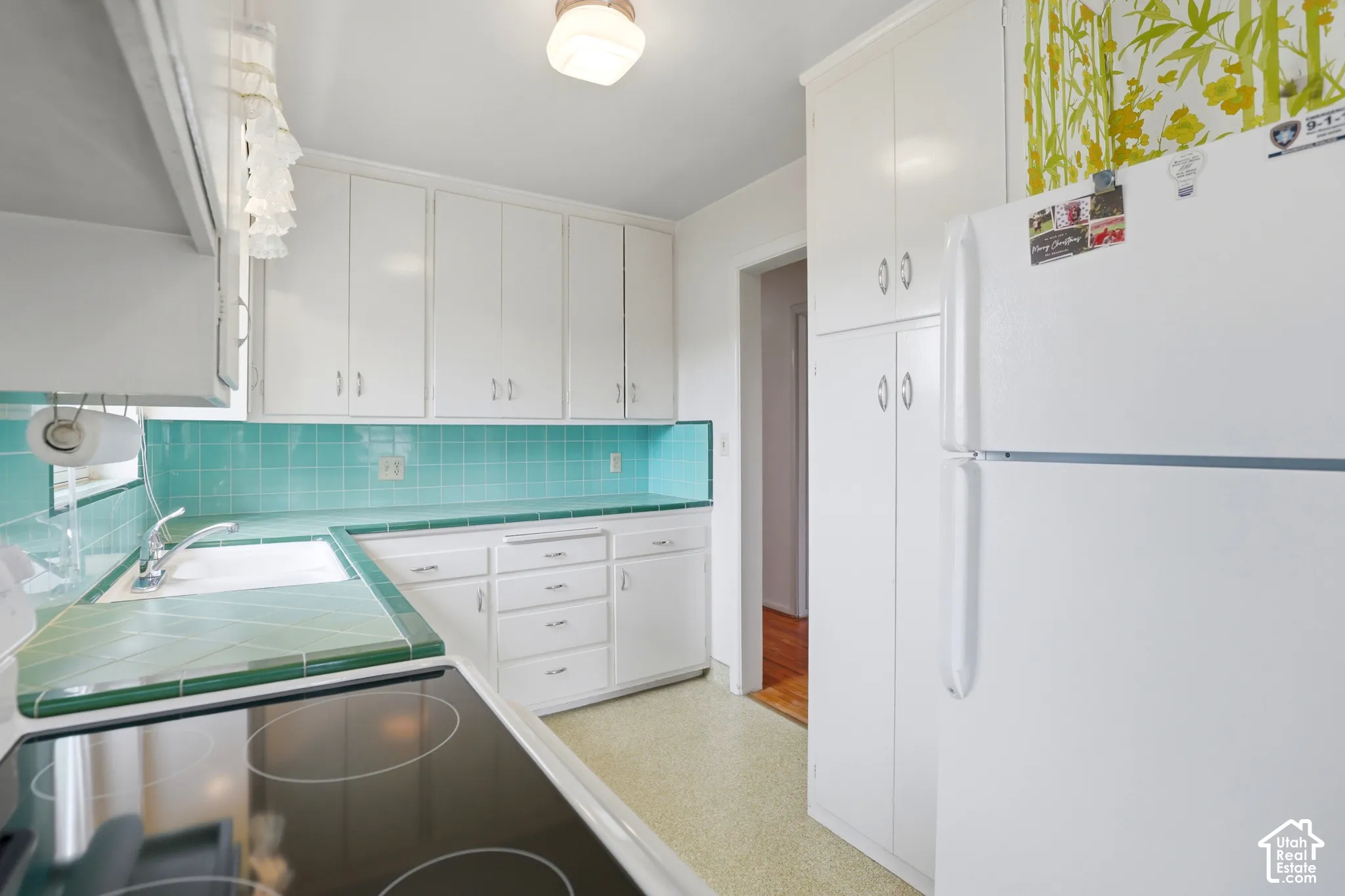 Kitchen featuring white cabinetry, floor-to-ceiling pantry storage, tiled countertops and backsplash, and an integrated stovetop