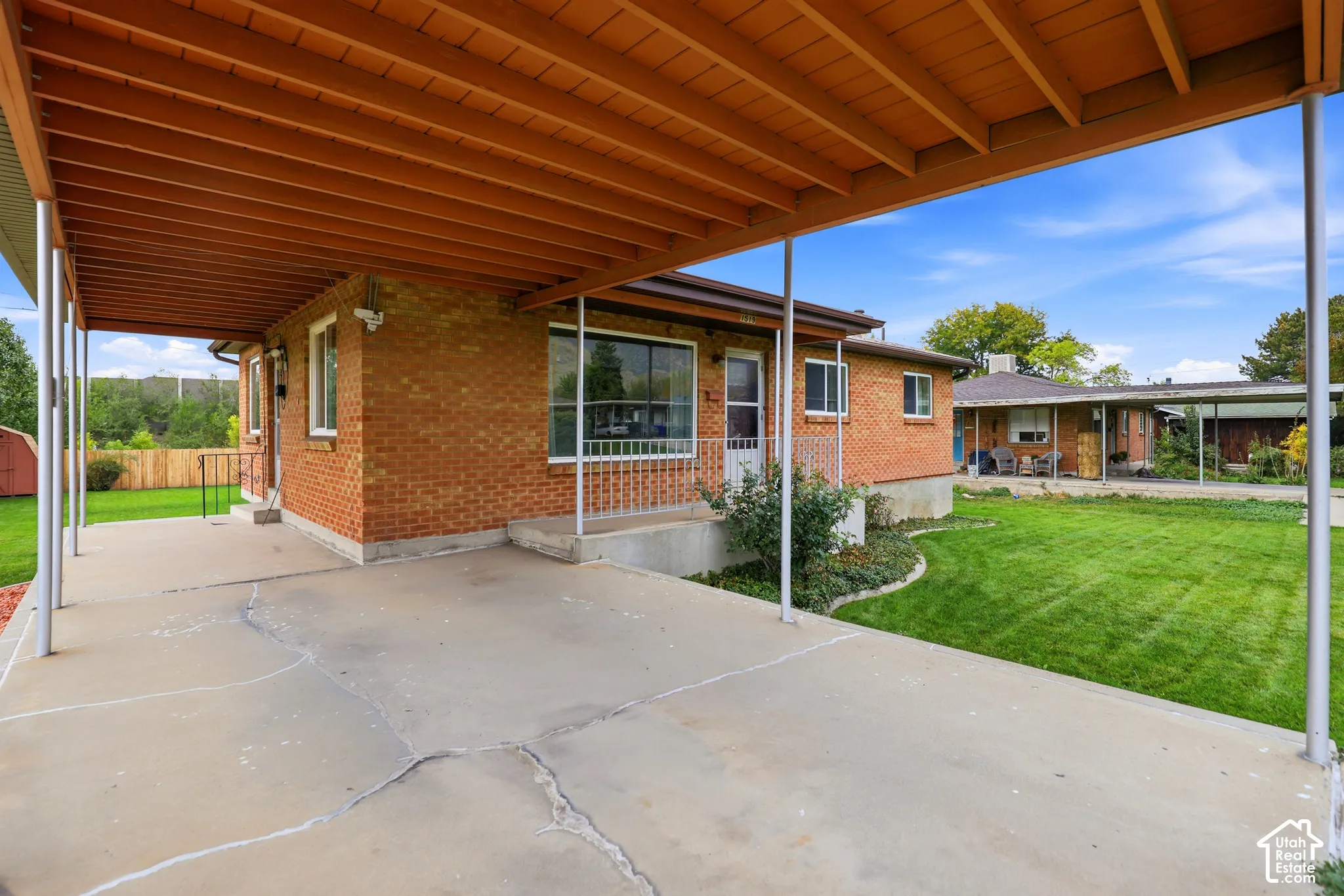 Exterior featuring a brick facade, covered concrete carport, manicured lawn, and metal roof supports