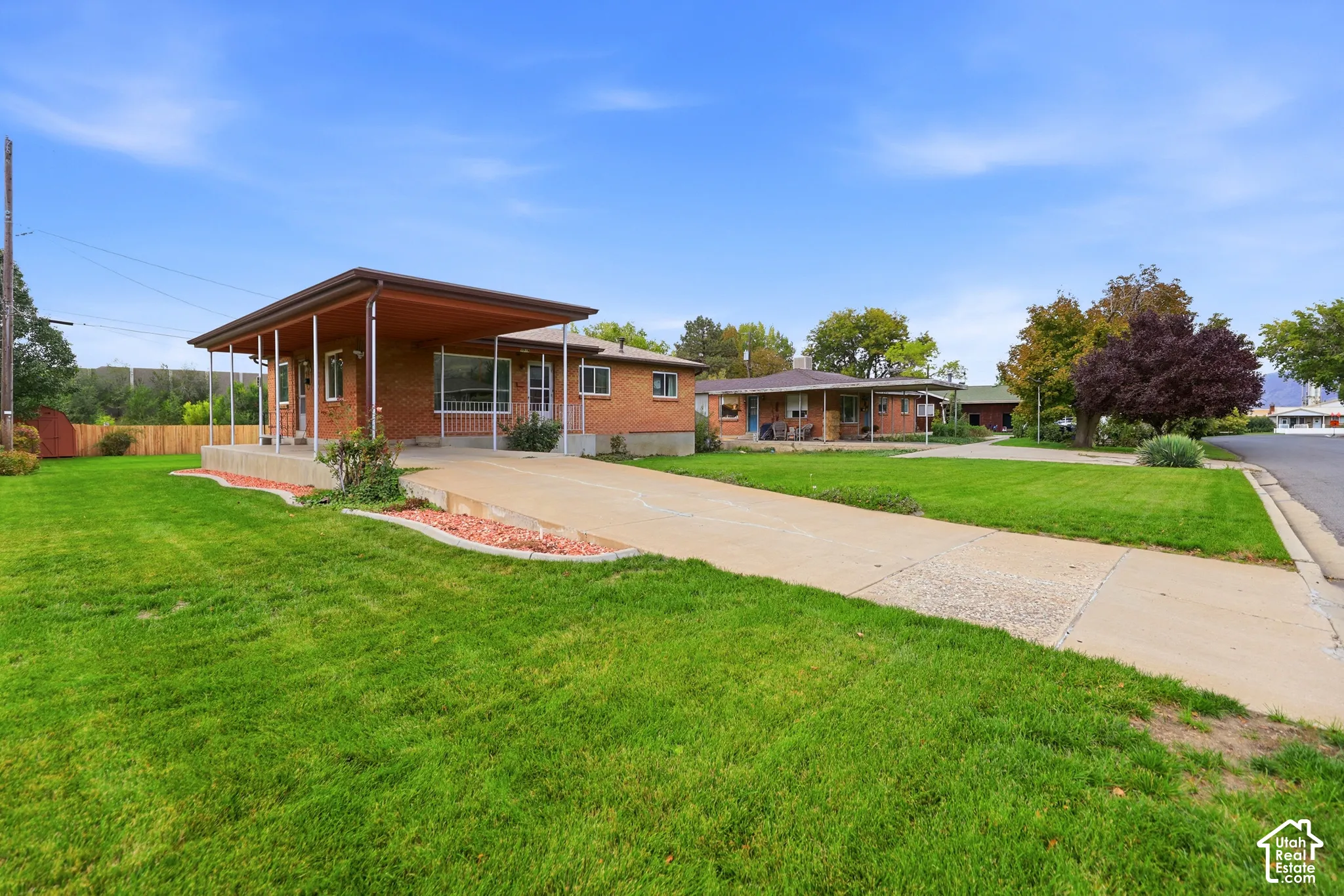 Brick exterior featuring a covered carport, concrete driveway, and landscaped lawn with stone-edged garden beds