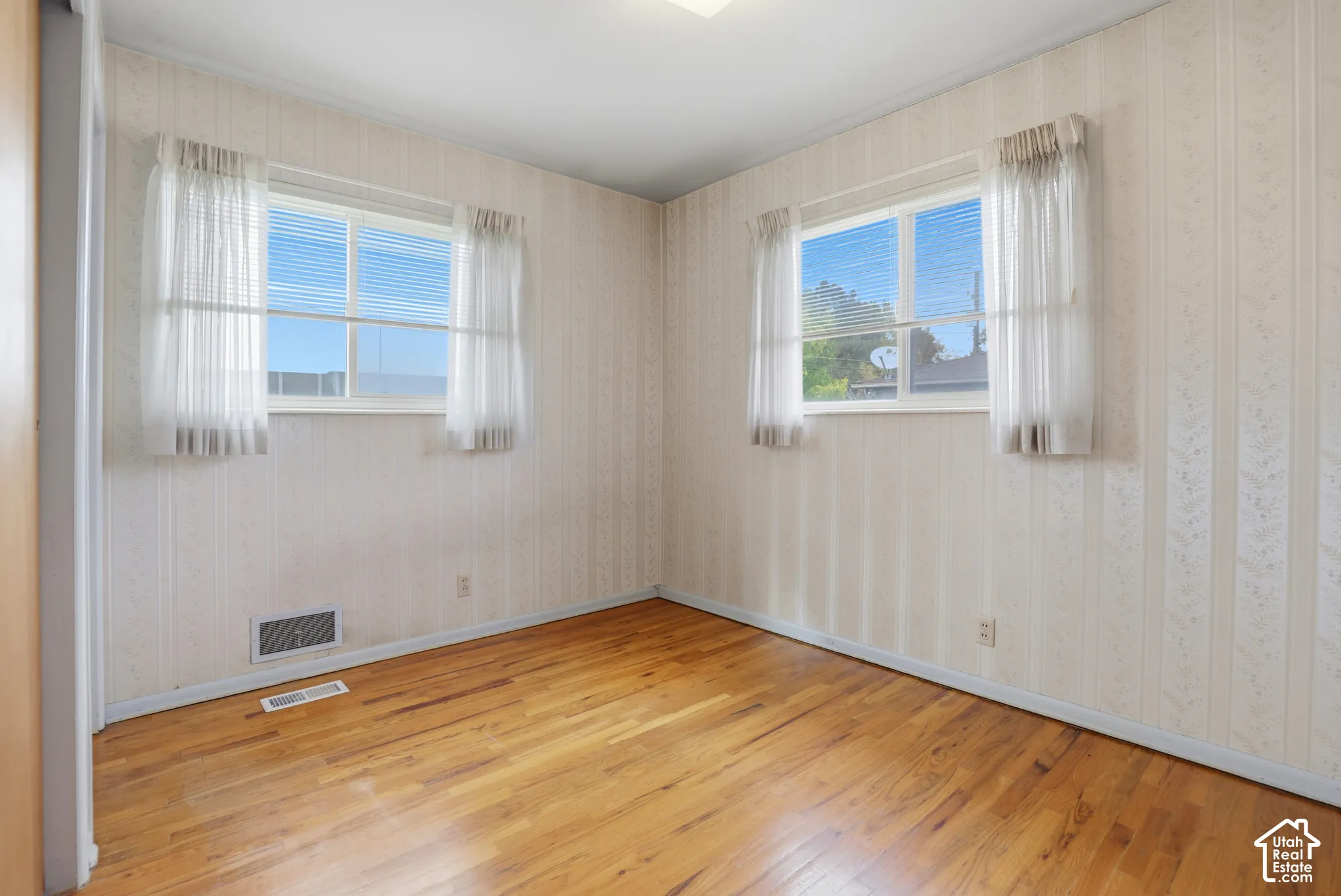 Room featuring wood-finish flooring, dual windows with sliding panes, and patterned wallpaper