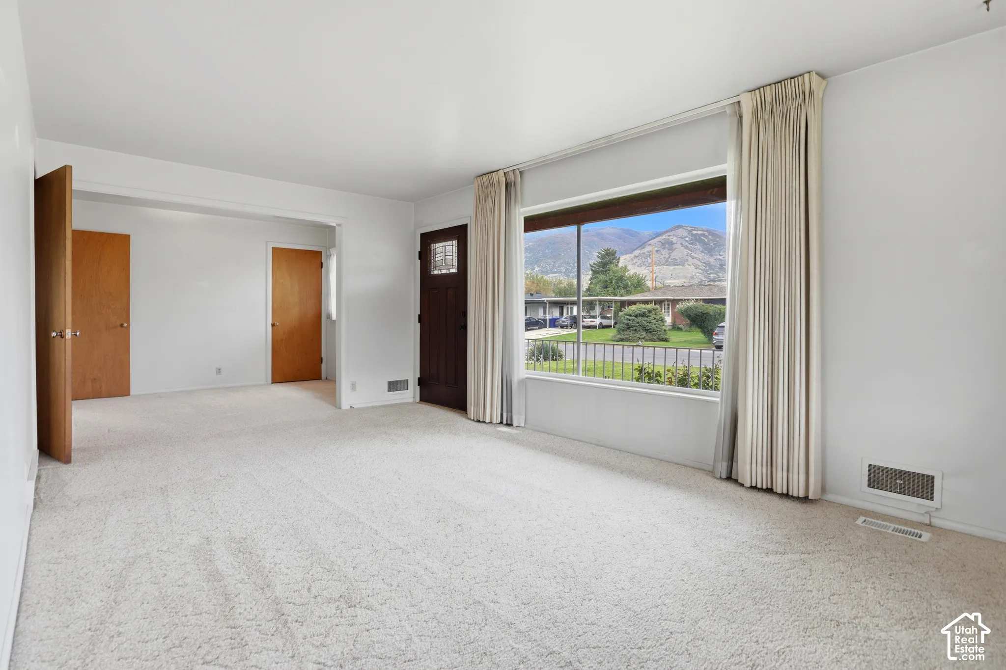 Large picture window with mountain backdrop, solid wood-finish entry door with glass pane, and neutral carpeting