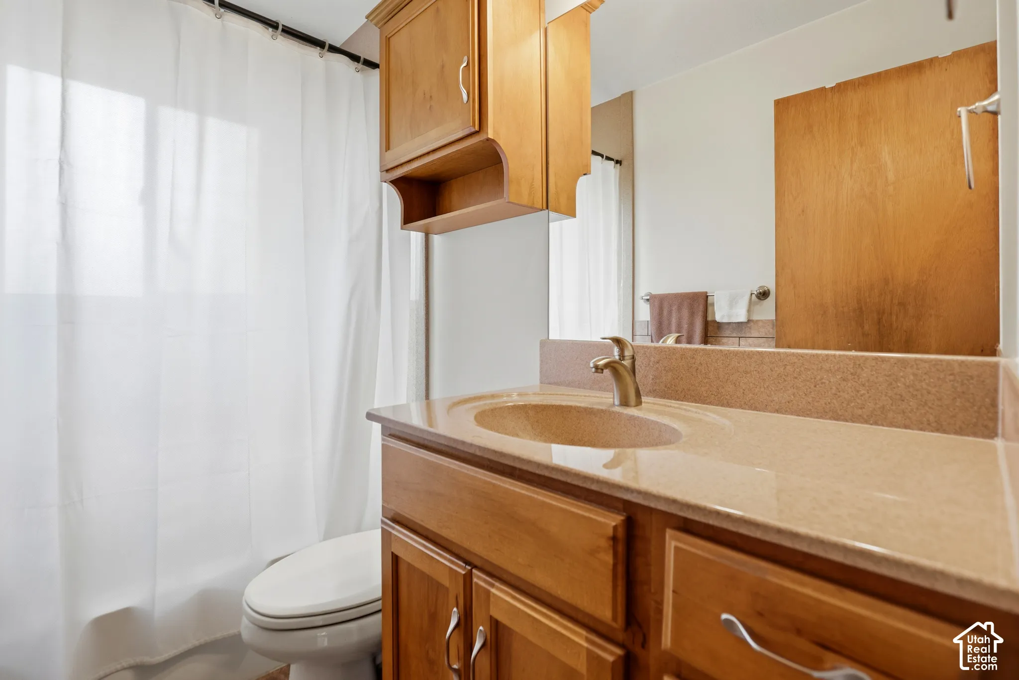 Bathroom vanity featuring warm-toned wood cabinetry, a solid surface countertop with an integrated basin, a wall-mounted medicine cabinet, and a metallic finish faucet