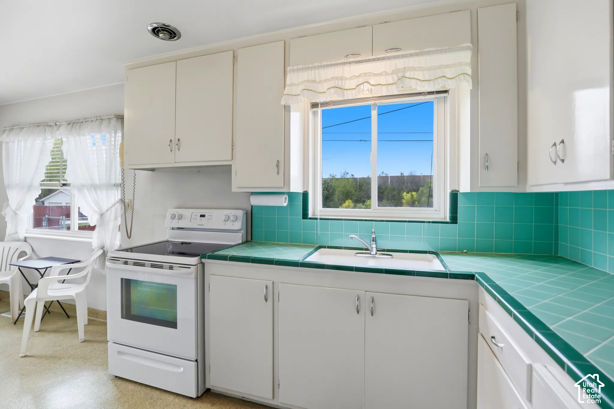 Kitchen featuring white cabinetry, teal tile countertops and backsplash, white freestanding oven, and a double-basin sink with a polished chrome faucet
