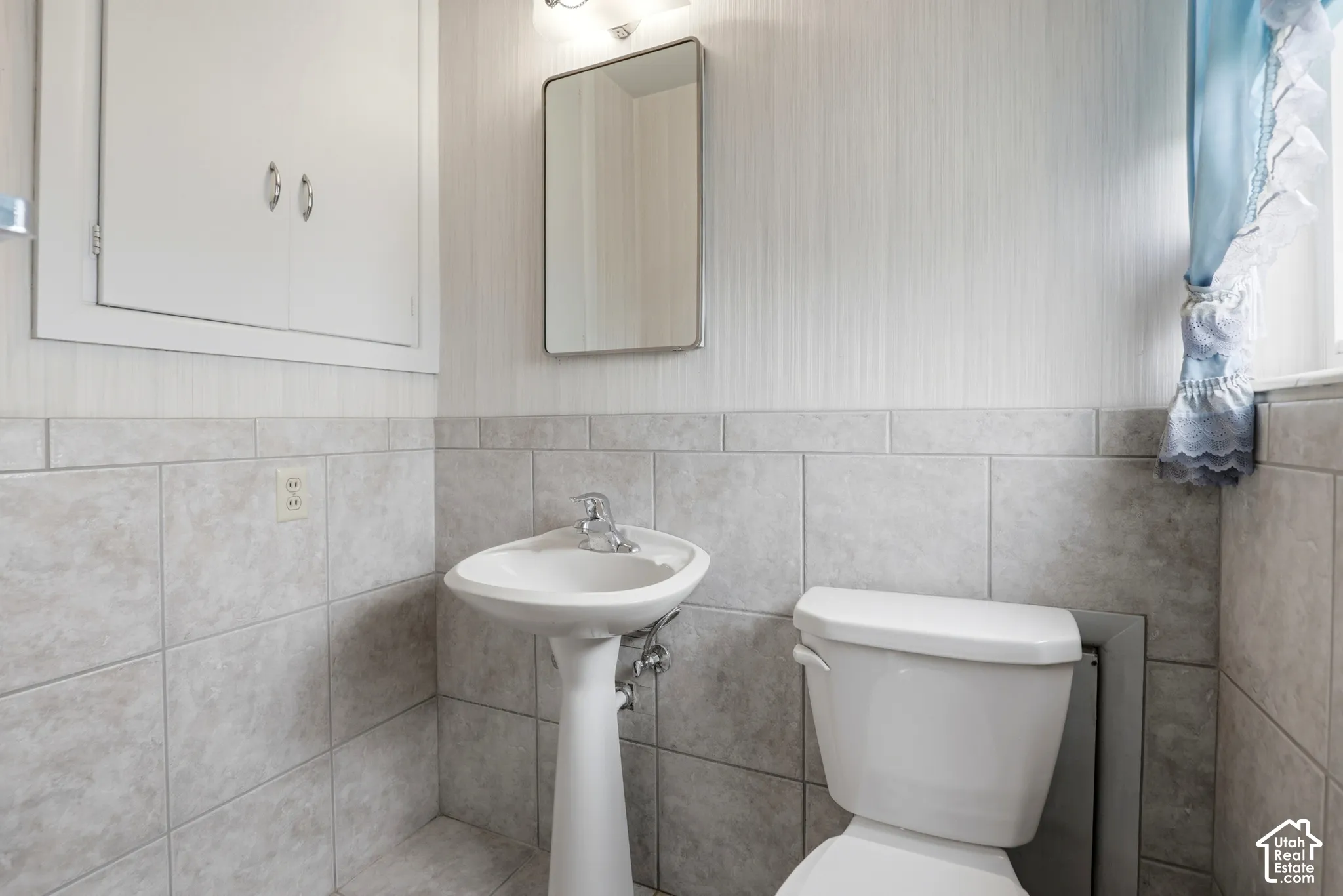 Bathroom featuring a pedestal sink with a chrome faucet, large-format tile wainscoting, built-in cabinetry, and a wall-mounted mirror