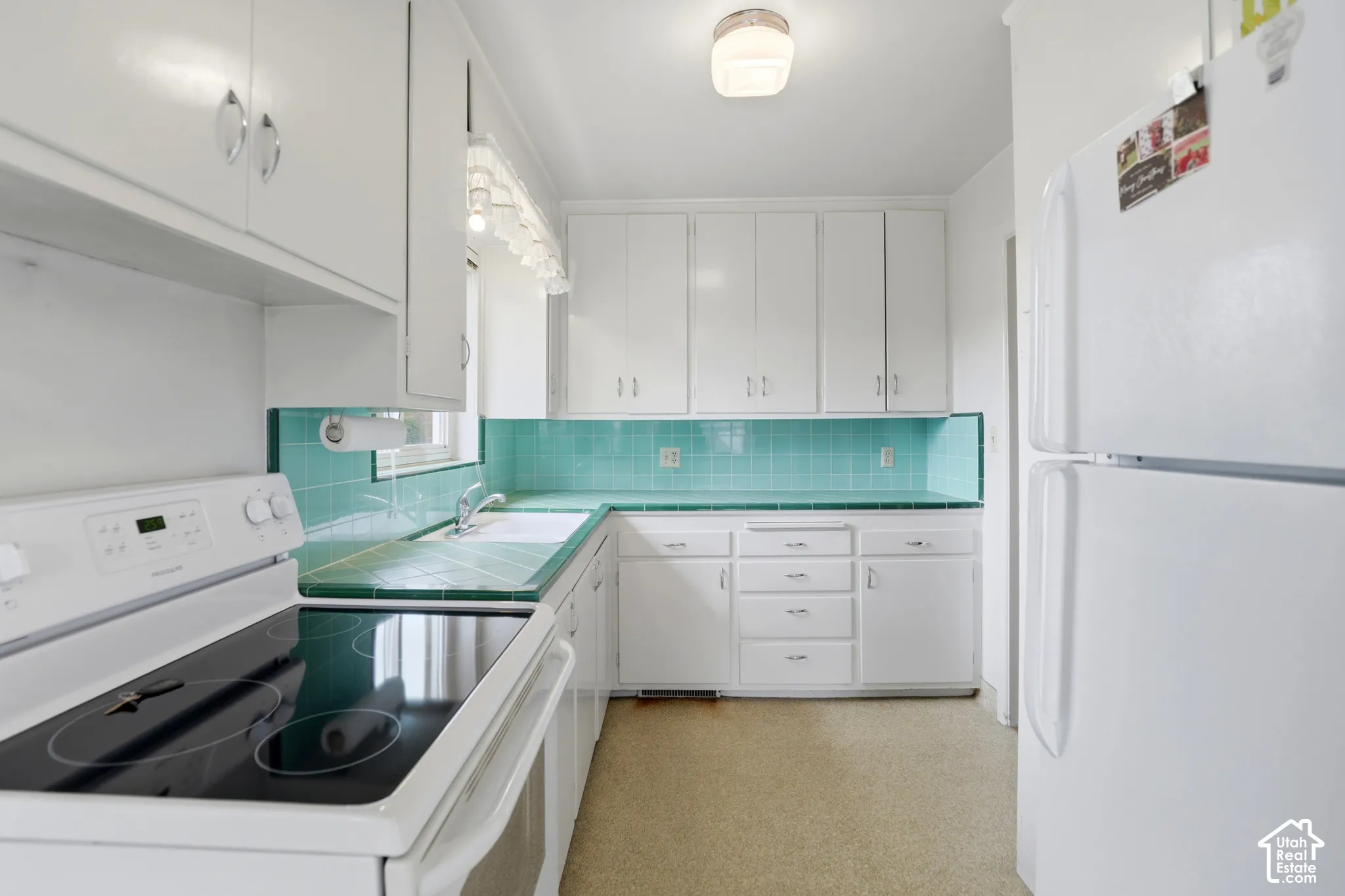 Kitchen featuring white cabinetry, turquoise tile countertops and backsplash, integrated sink, and glass-front flush-mount ceiling lighting