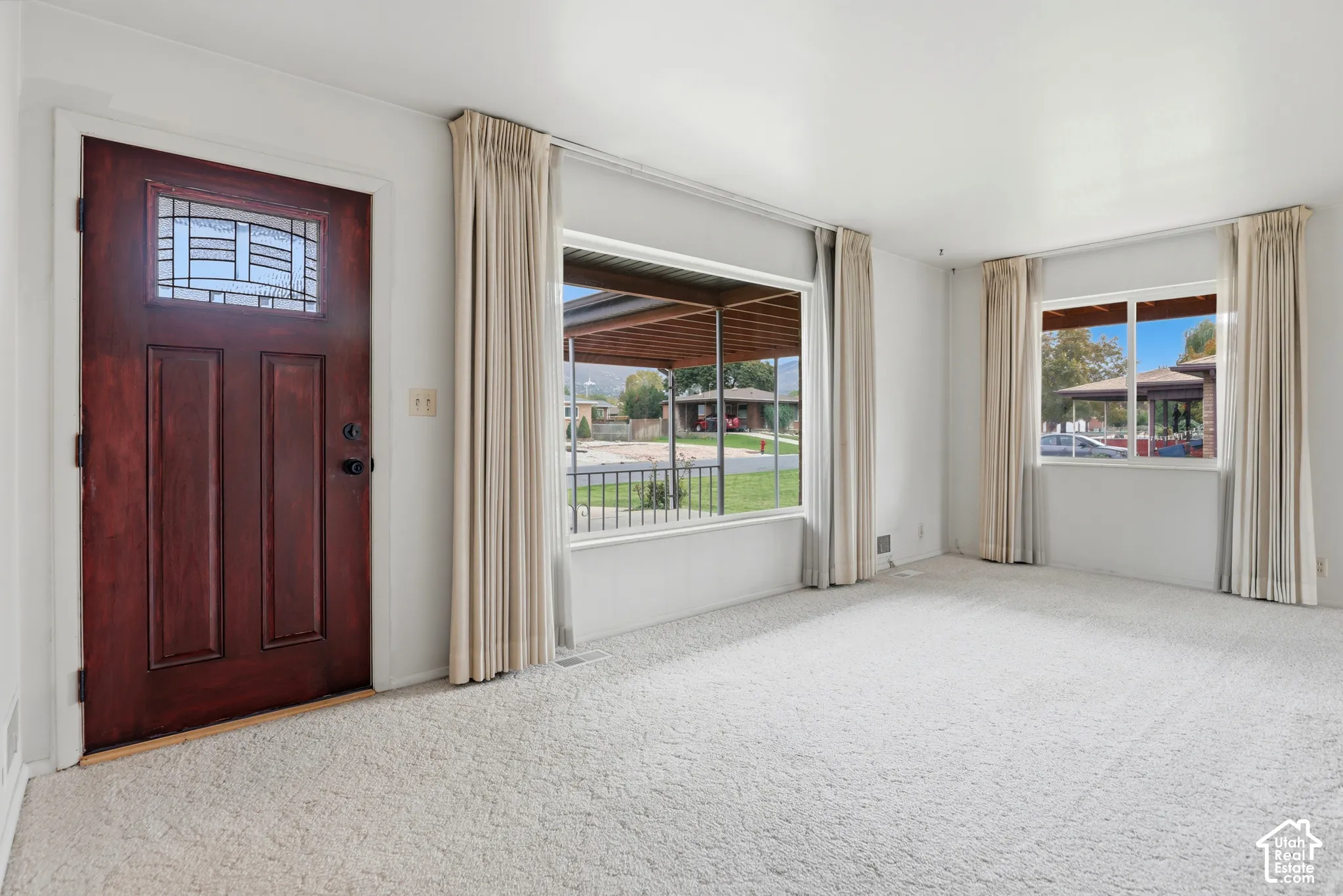 Solid wood entry door featuring a decorative glass inset, large picture windows, and wall-to-wall carpeting