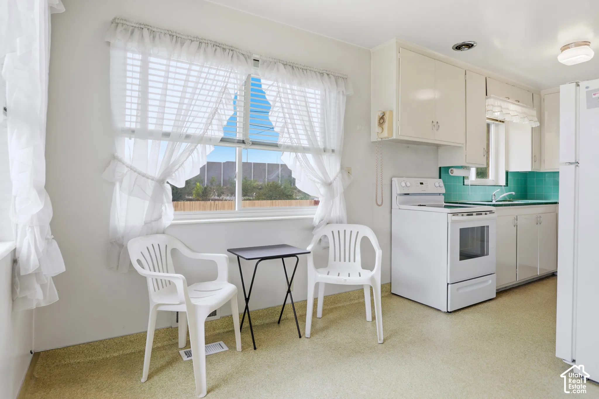 Kitchen featuring solid-surface cabinetry, white electric range, teal backsplash, and bright window with natural light