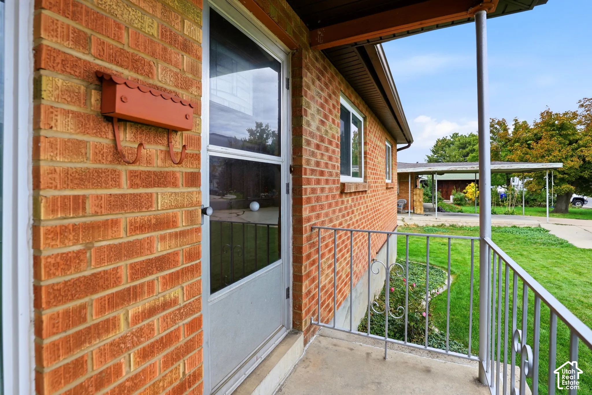 Exterior entrance featuring a brick facade, covered porch with metal railing, and a wall-mounted metal mailbox
