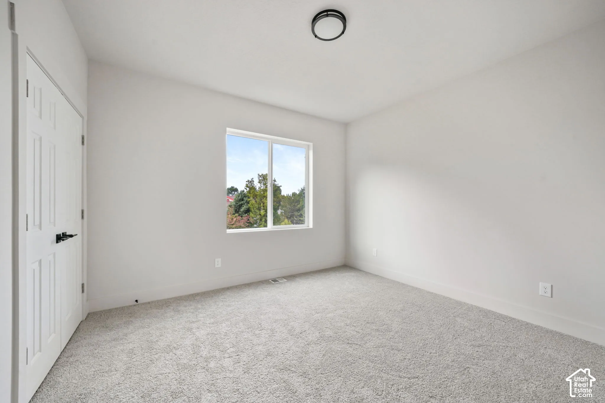 Neutral-toned wall paint, plush carpeting, single-pane window, and a double-door closet featuring matte black hardware