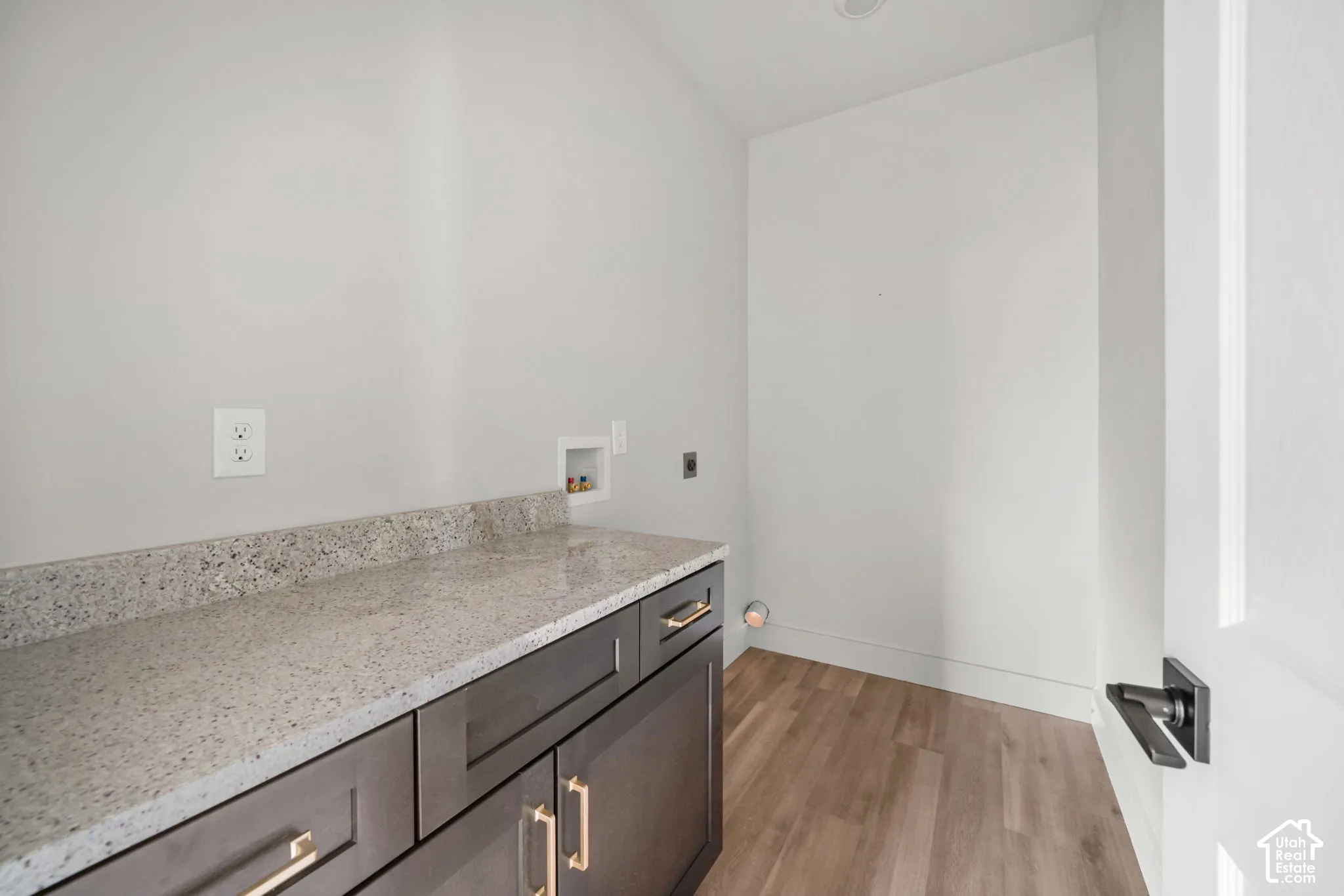 Utility area featuring shaker-style cabinetry, stone-finish countertops, wood-finish flooring, and matte-finish hardware