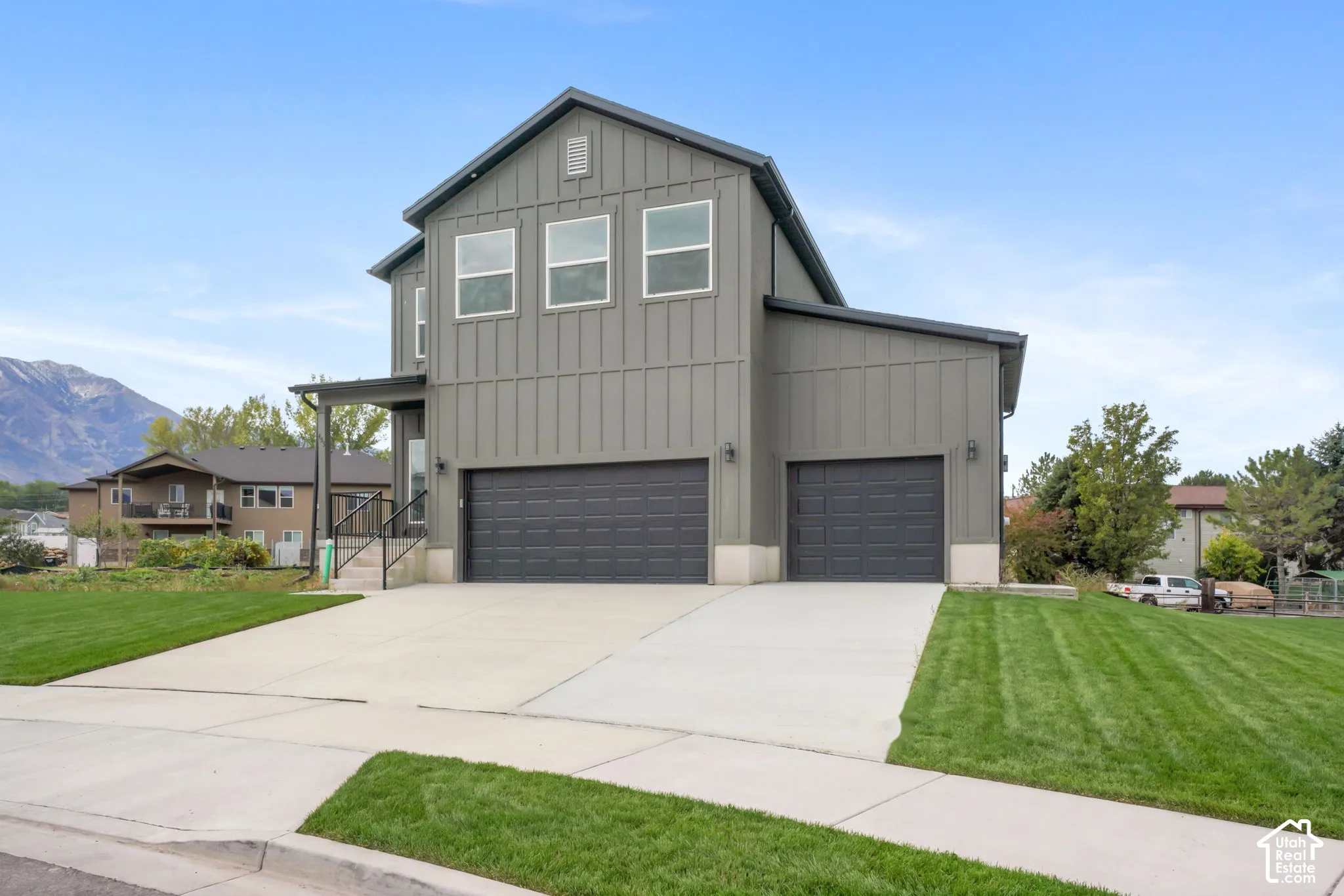 Two-story exterior featuring vertical siding, a three-car garage, concrete driveway, and manicured lawn