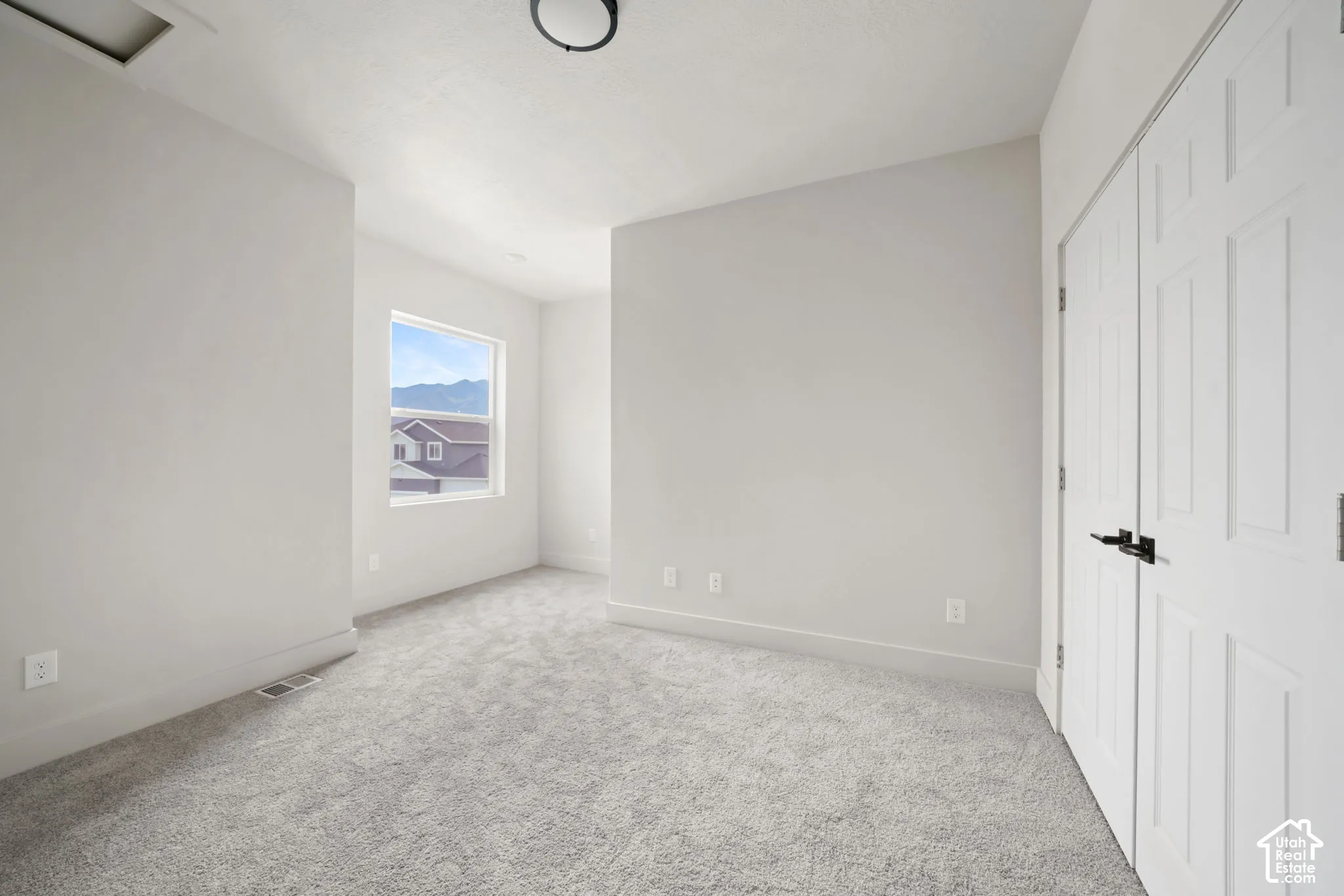 Neutral-toned interior featuring wall-to-wall carpeting, dual-panel closet doors with matte black hardware, and a single-hung window with mountain scenery