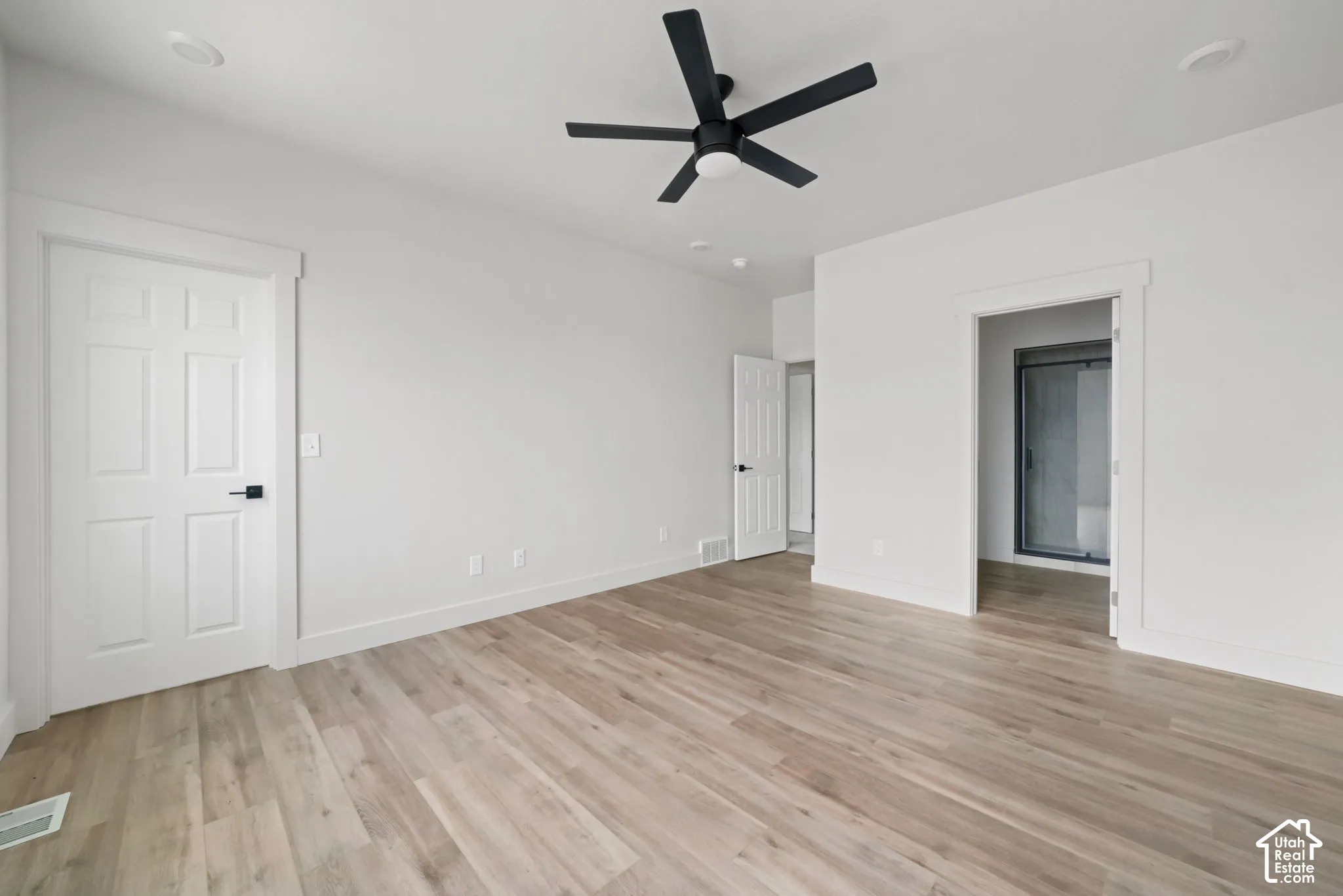 Room featuring wood-finish flooring, a matte black ceiling fan, six-panel interior doors with matte black hardware, and recessed lighting
