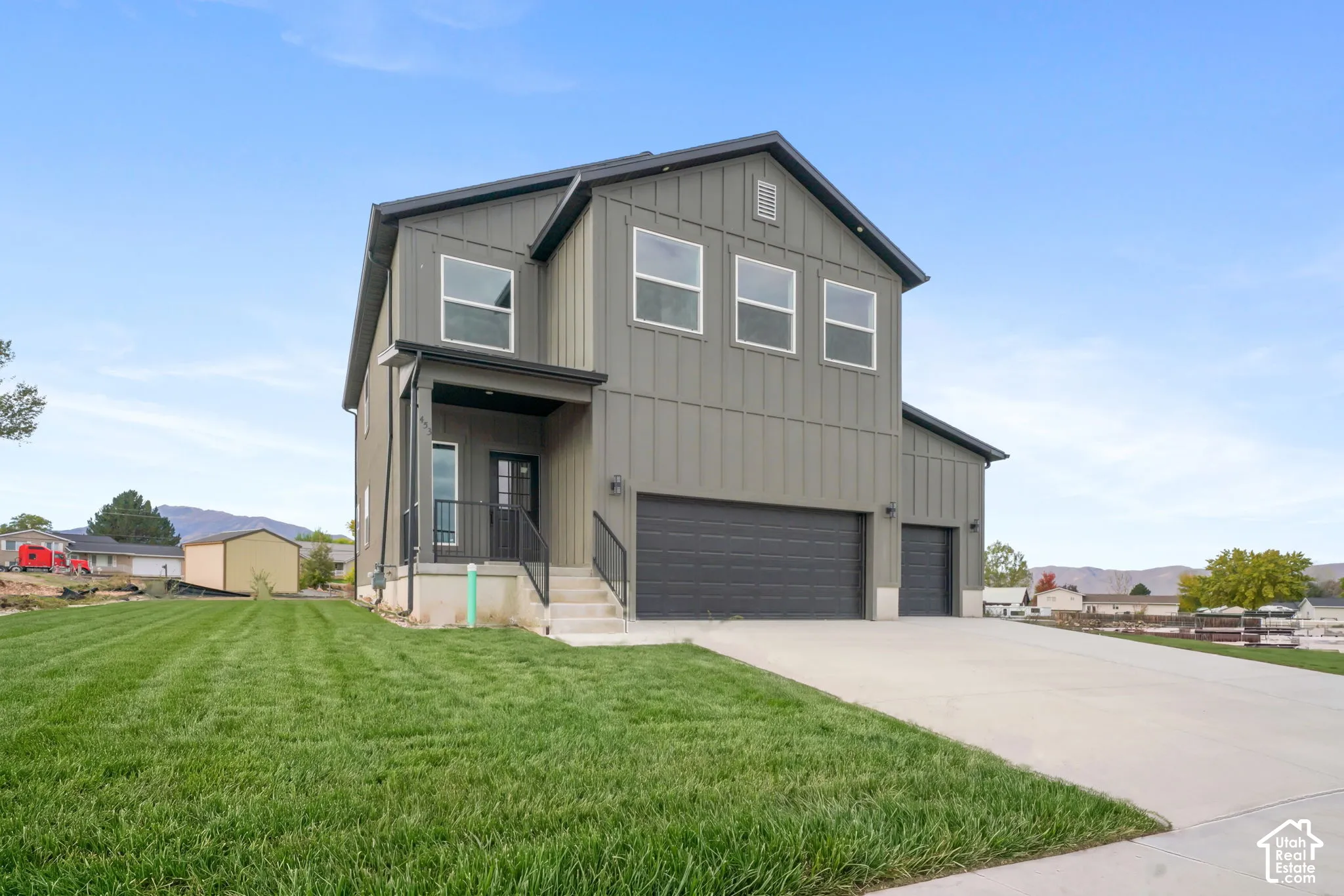 Two-story exterior featuring vertical siding, a three-car garage, concrete driveway, and an elevated front porch with metal railing