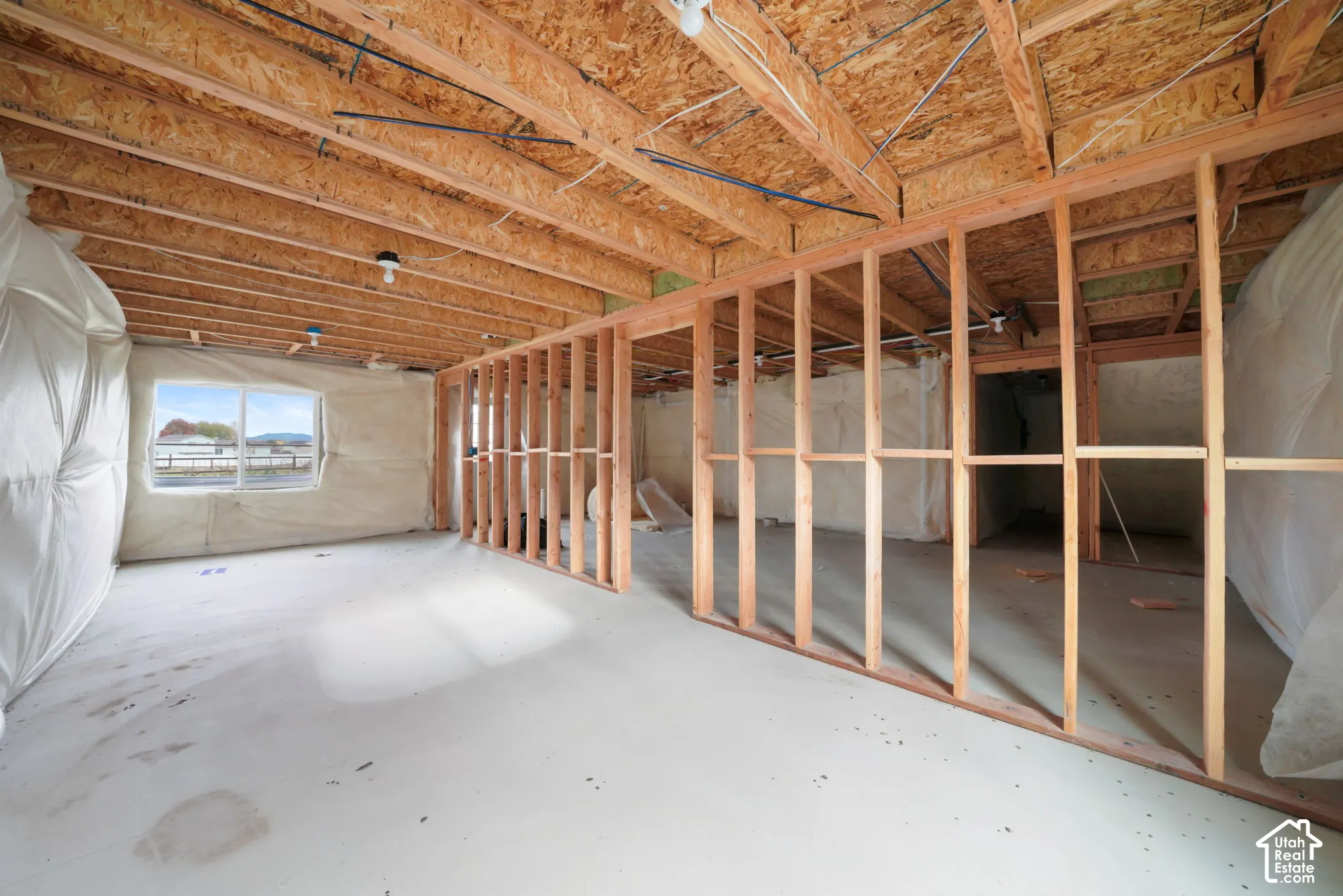 Unfinished interior space featuring exposed wood-framed walls, an open-joist ceiling, concrete flooring, and a single-pane window